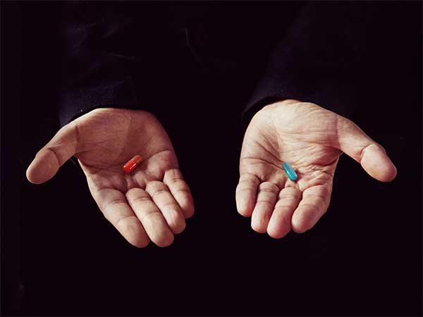 Hender som holder rød og blå pille.