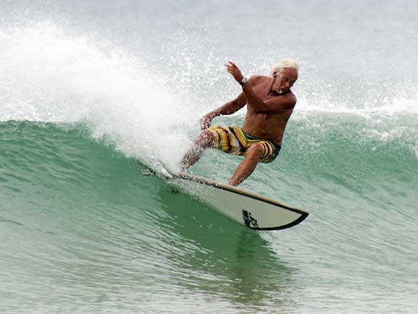 Eldre mann surfer på bølge.