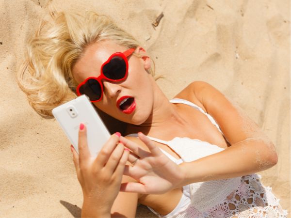 Kvinne på stranden ser på mobiltelefon.