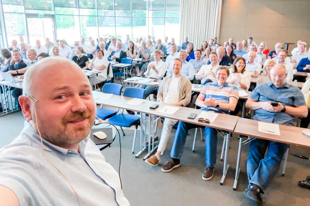 Fotografi av smilende foreleser foran et fullt klasserom.